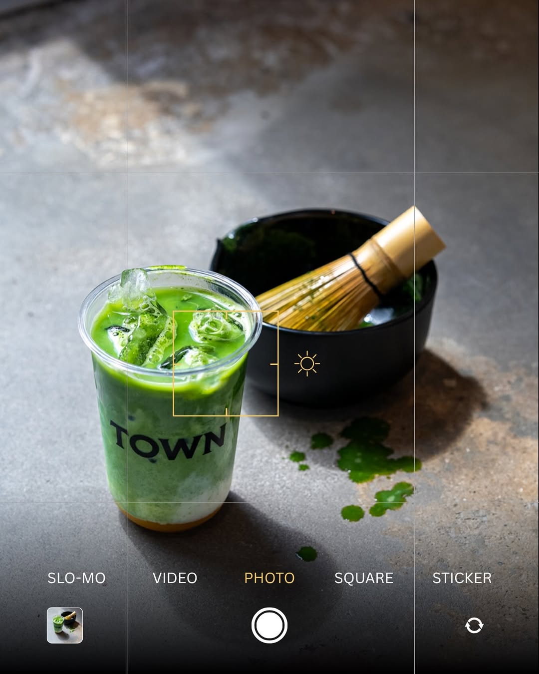 Iced matcha in a Town cup next to a bamboo whisk and matcha bowl