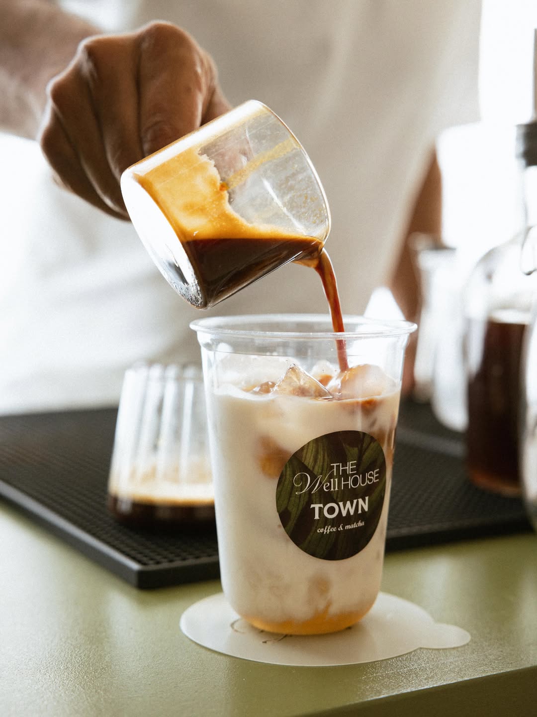 Espresso poured over an iced latte in a Well House × Town cup